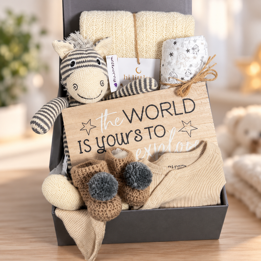 Unisex baby gift hamper in a grey baby keepsake box containing a Hippychick cellular baby blanket, a Wilberry Knitted Zebra soft toy, a Ziggle elephant print large baby muslin square, a pir of hand crocheted baby booties with pompoms, a neutral cotton baby sleepsuit and matching bay knot hat and a large nursery plaque.