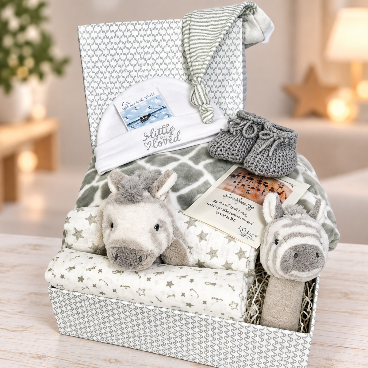 This zebra themed baby hamper comes in a grey and white  baby keepsake box and contains 2 soft zebra baby rattles, a grey baby blanket with a grey and white giraffe pattern, a pair of grey baby booties, a wish bracelet, a baby grey knot hat and a white cotton baby hat along with 2 baby muslin squares.