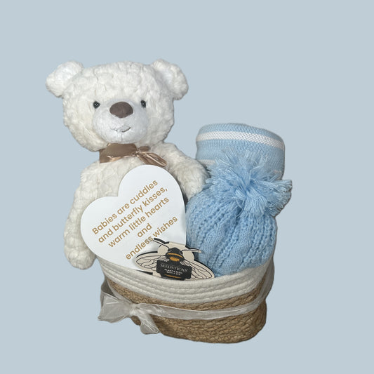 Gift hamper with cream teddy, blue and white striped baby blankets, blue baby pompom hat and white hear with gold coloured text.