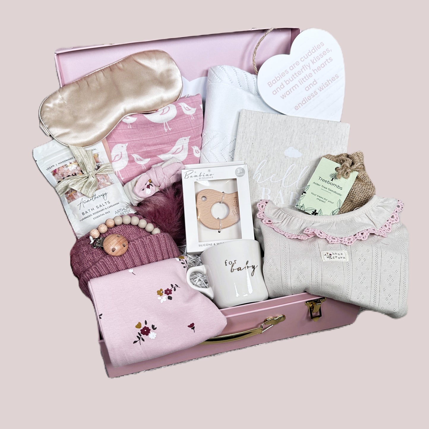 Gift box with baby-themed items including a hat, blanket, and sleep mask on a pink background