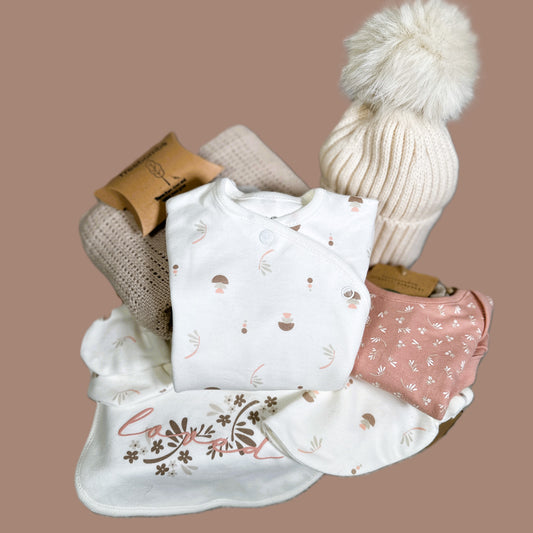 Baby girl hamper with baby clothes, hat, and blanket on a brown background