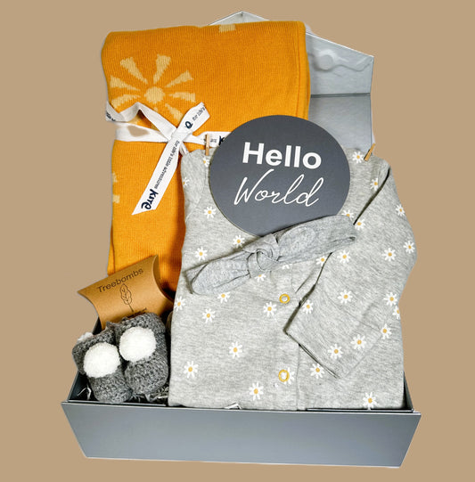 New baby girl hamper gift box containing a cotton baby sleepsuit with a white and yellow daisy print and a cotton baby headband. An Organic cotton baby blanket with a sunshine print.