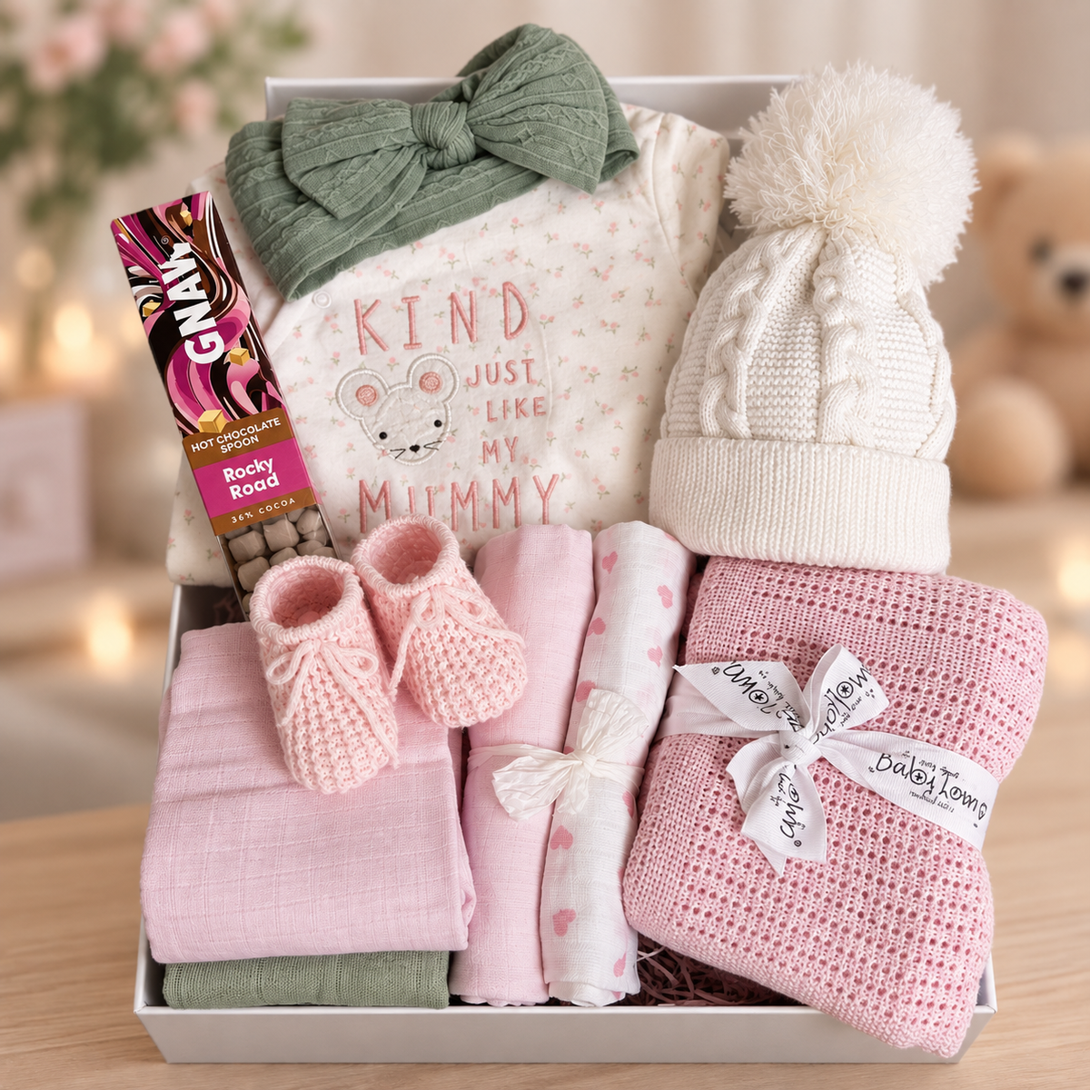 Baby Girl hamper with sleepsuit green hairband white baby hat, pink blanket and pink booties.