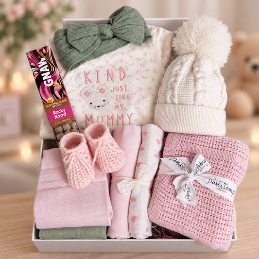 Baby Girl hamper with sleepsuit green hairband white baby hat, pink blanket and pink booties.
