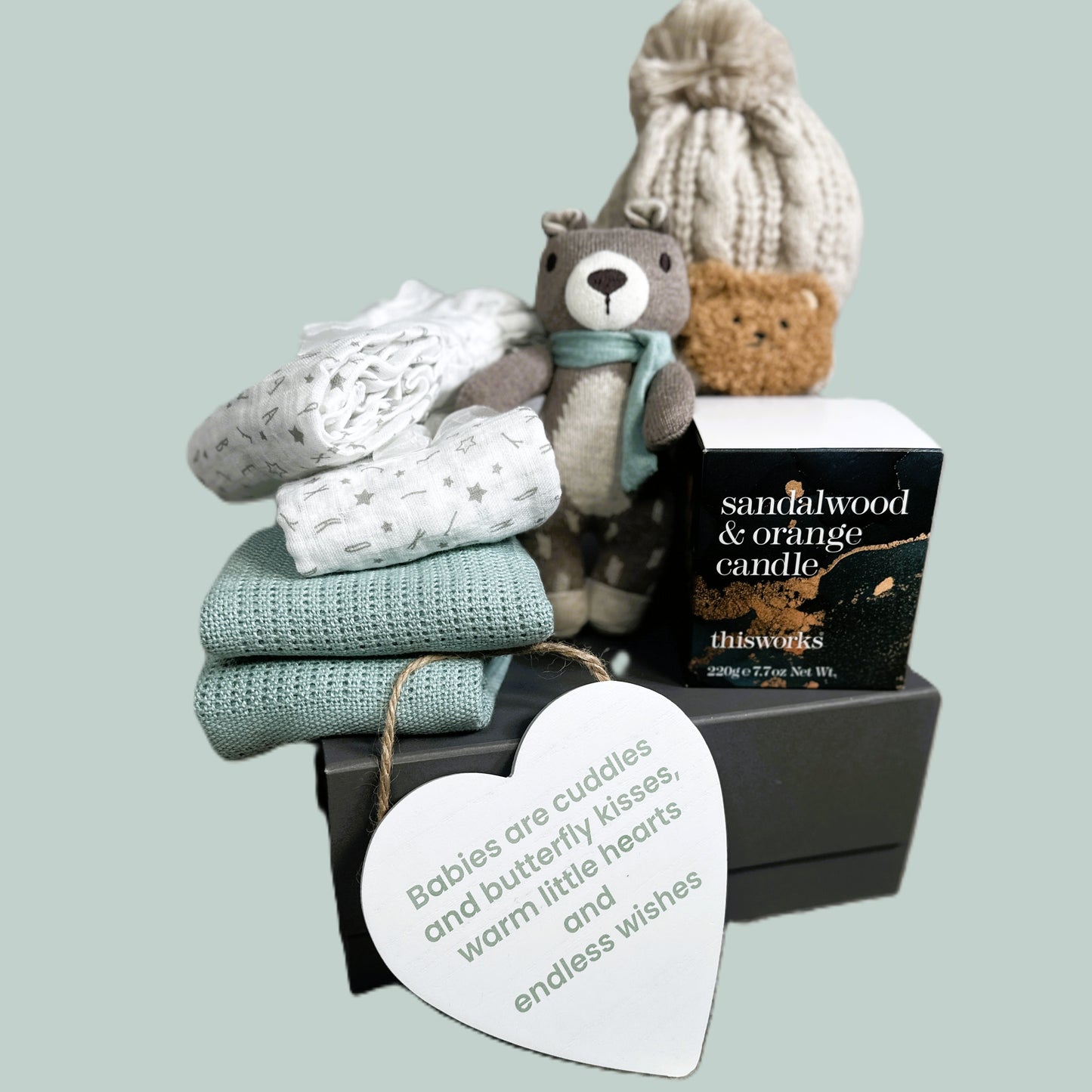 Baby shower gift with teddy bear, baby blanket and muslins, and candle on a light blue background