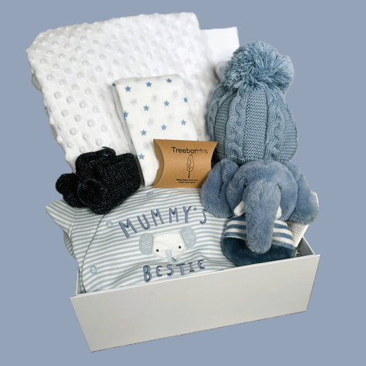 Baby gift set with clothing, blanket, and toys in a box on a light blue background