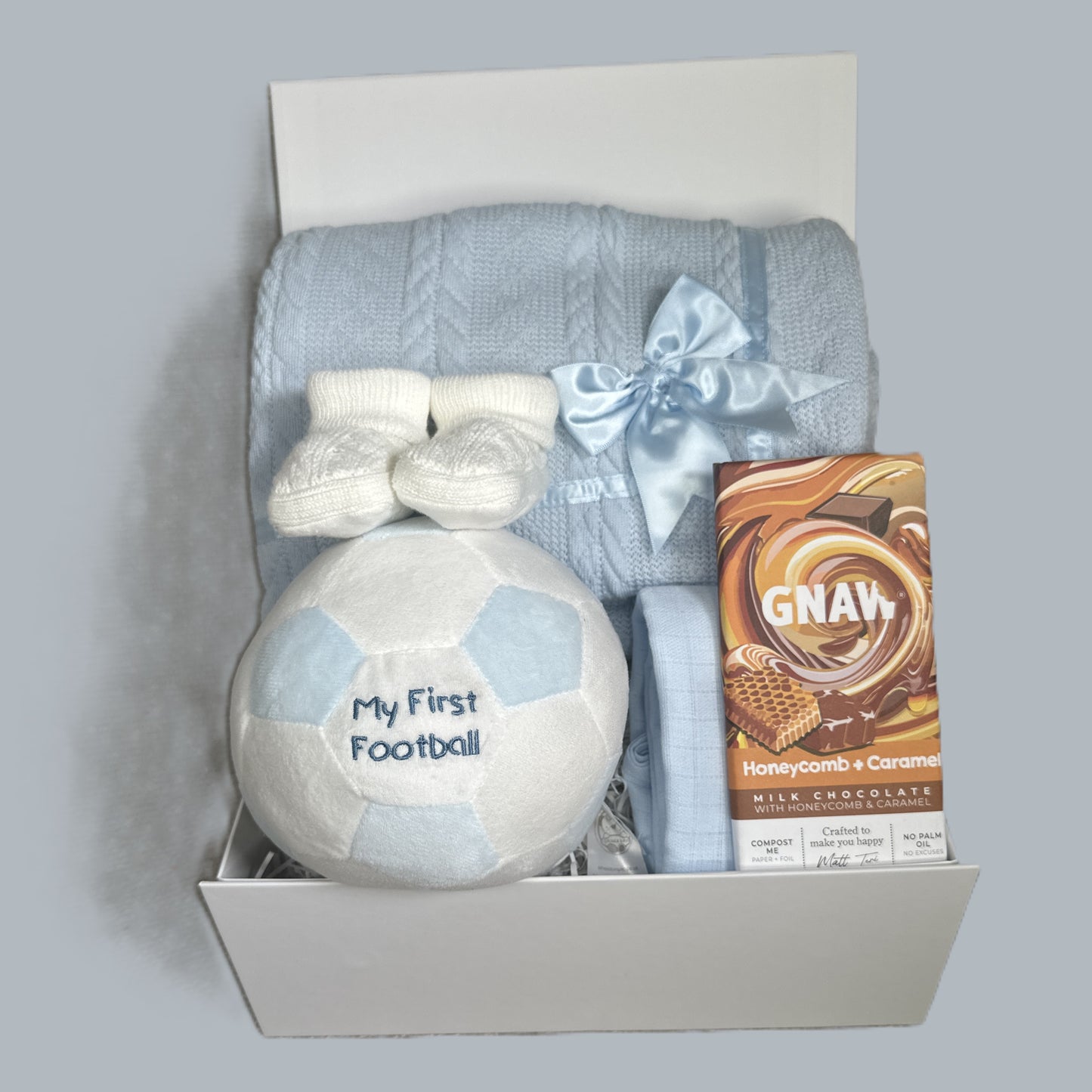 Baby gift set with 'My First Football', baby shoes, blanket, and chocolate bar in a baby keepsake box.