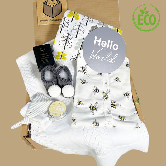 This Unisex new baby gift is full of eco friendly gifts for the new baby and the new mummu including a white cotton soft baby blanket, and organic cotton bee print baby romper, a pair og grey crocheted baby booties with white pompoms, a lagre muslin baby swaddle blanket, a Unnaaty ssoya wax candle, a pot of vanilla vegan lip balm, a grey and white striped baby knot hat and a "Hello world" baby photography disc.