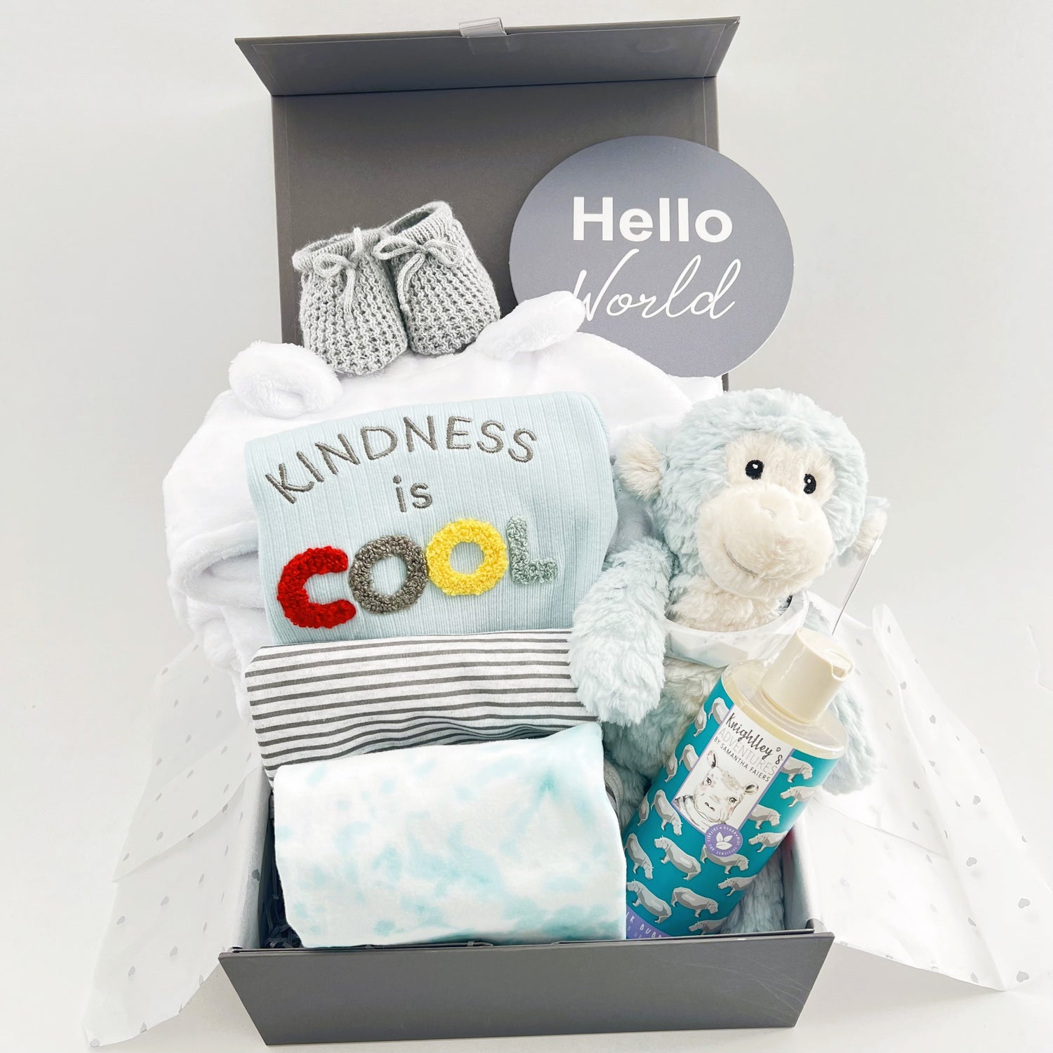 New baby boy hamper gift box containing a blue monkey soft baby toy, A set of three organic botton baby body suits, one with the wording " kindness is cool", a white baby hooded dressing gown,  Knightley's Adventure bath wash, a pair of grey baby booties and a baby photography plaque withe the words "Hello world" all in a grey magnetic baby keepsake box.