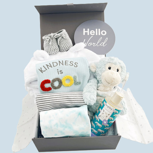 New baby boy hamper gift box containing a blue monkey soft baby toy, A set of three organic botton baby body suits, one with the wording " kindness is cool", a white baby hooded dressing gown, Knightley's Adventure bath wash, a pair of grey baby booties and a baby photography plaque withe the words "Hello world" all in a grey magnetic baby keepsake box.
