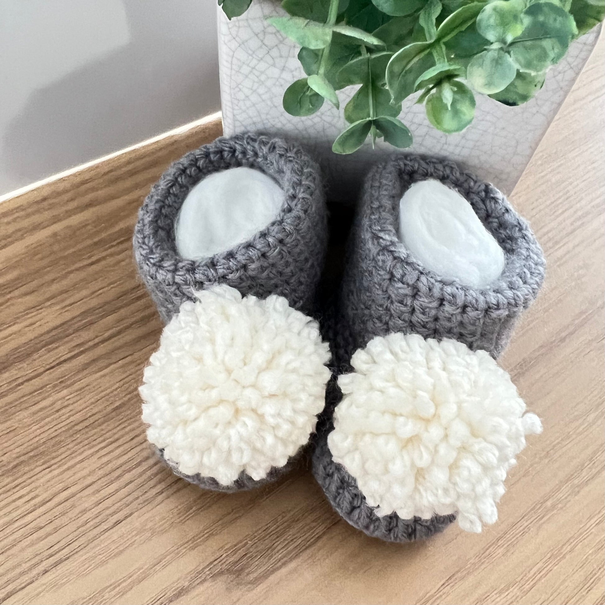 crocheted baby booties in grey cotton with a white pompom.