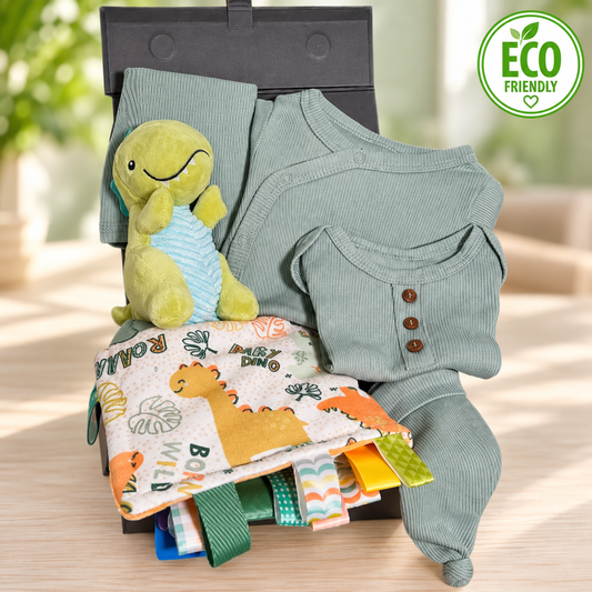 A dinosaur themed baby hamper gift with a Mary Meyer dinosaur print Taggie blanket, a Mary Meyer green dinosaur baby rattle and a sage green cotton layette set.