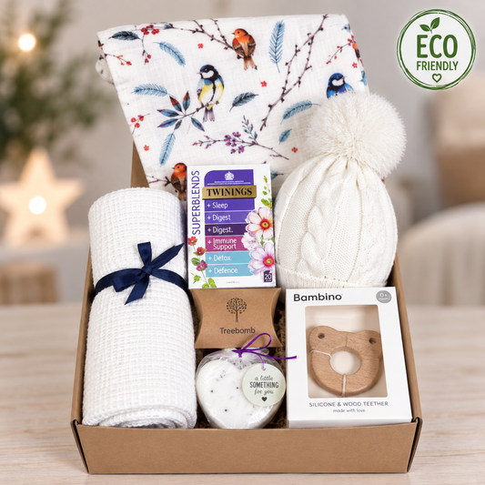 Eco friendly newborn baby girl gift includes a large whie baby muslin with a bird print, a white cottoncellular baby blanket, a baby pompom hat, a wooden bird baby teether, a heart shaped bath bomb and some sleepy tea for the new parents.