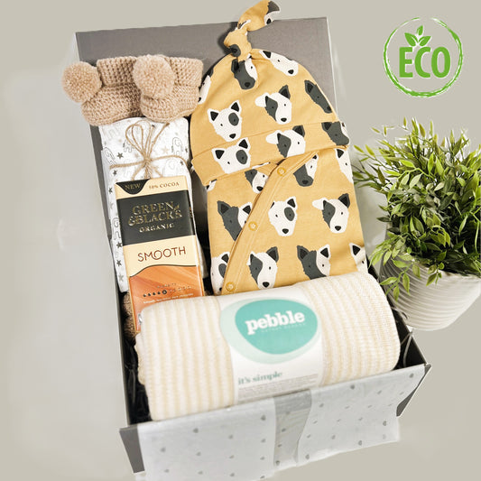 Mustard and cream unisex new baby gift hamper containing a GOTS certified organic cotton baby romper with a dog face print, fold over cuffs and feet with a matching baby knot hat, a hand knitted cotton baby blanket, an elephant print baby muslin, a pair of crocheted baby booties, a bar of green and Blacks organic "smooth" chocolate all in a grey magnetic baby keepsake case.