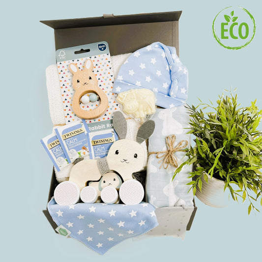 Newborn baby boy gift containing an FSE wooden Baby rattle and pull along toy, a blue bunny print large muslin swaddle, a cotton cellular baby blanket in white, a matching baby knot hat and dribble bib plus some chocolate and teabags for the ne parent/s.
