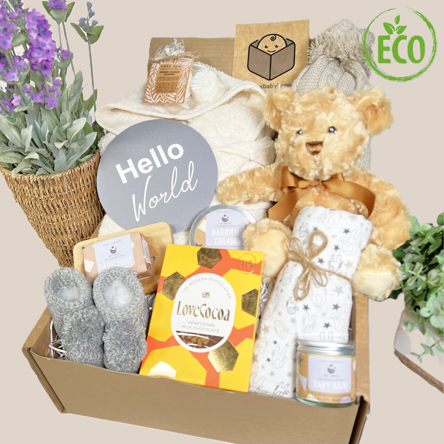 Gorgeous neutral new mummy and baby hamper containing eco friendly baby toiletries, a cotton baby dressing gown with hood, an eco friendly teddy bear baby toy, a baby pompom hat, a bar of chocolate and some shower spa steamers for Mummy, a pair of hand crocheted baby booties with pompoms,q muslin square and a "Hello World" plaque.