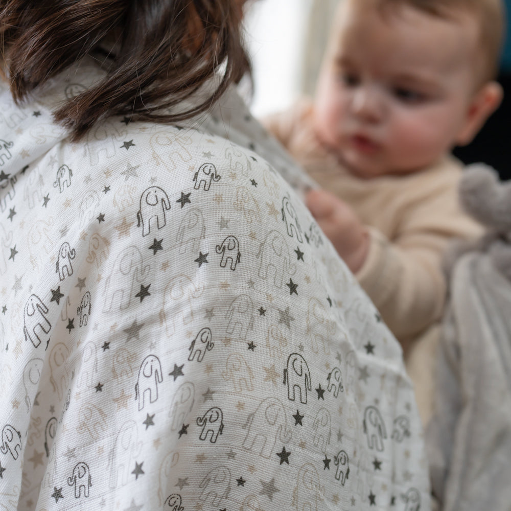White baby muslin fabric with a repeating pattern of small elephant silhouettes and stars in light grey and beige and a baby.
