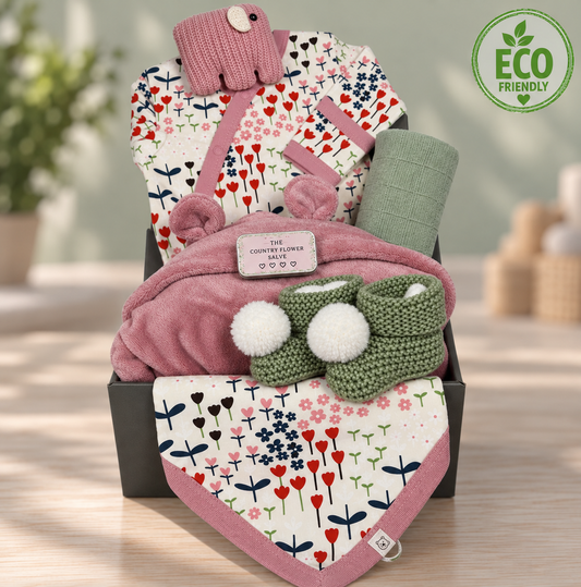 Stunning baby girl hamper with a organic cotton baby romper and baby dribble bis in  a flower print. Green  crocheted baby bootees  with white pompoms, a green muslin square, a pink baby dressing gown, a Pebblechild elephant baby rattle and a tin of moisturising salve.