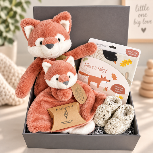 Neutral New Baby shower gift full of eco friendly items including  a cloth baby book, an Ebba Fox soft toy and Ebba fox baby comforter, a cotton baby bib and a pair of crocheted baby booties with pompoms.