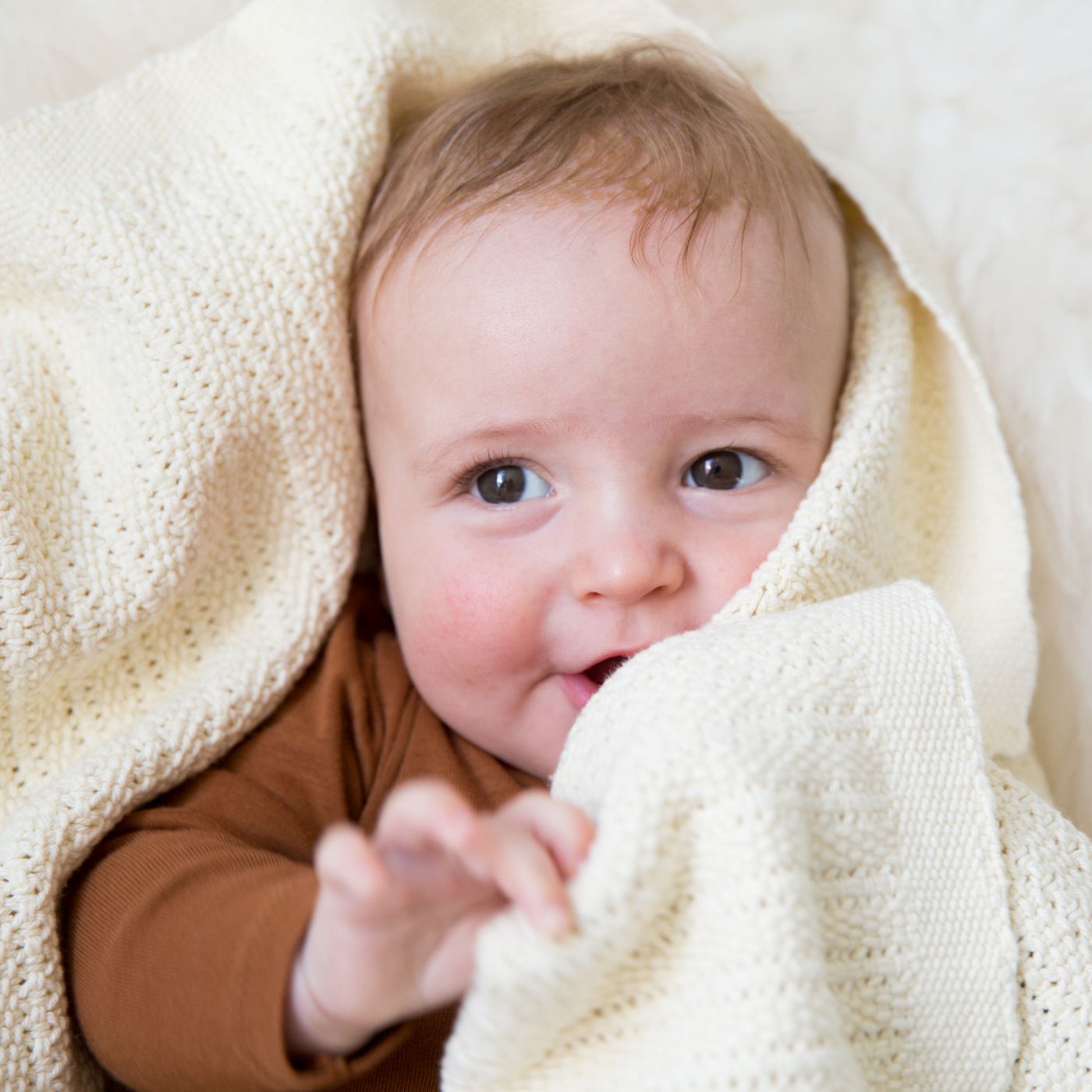 Baby peeking out from under a almond coloured cellular baby blanket