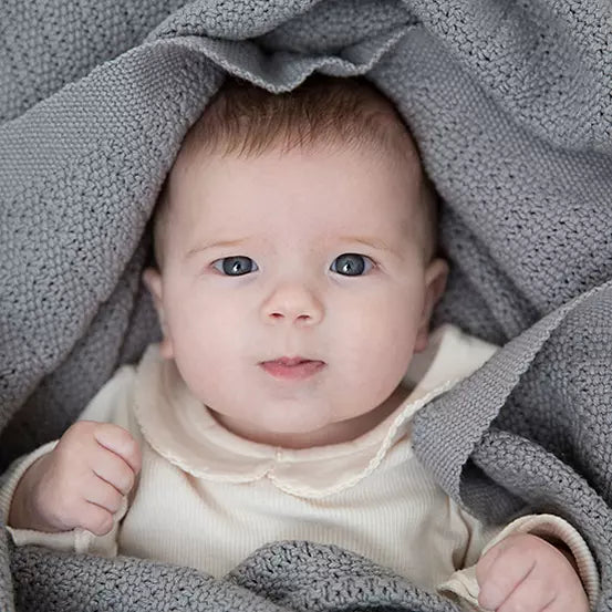 A close-up of a baby wrapped in a soft grey cotton cellular baby blanket. 