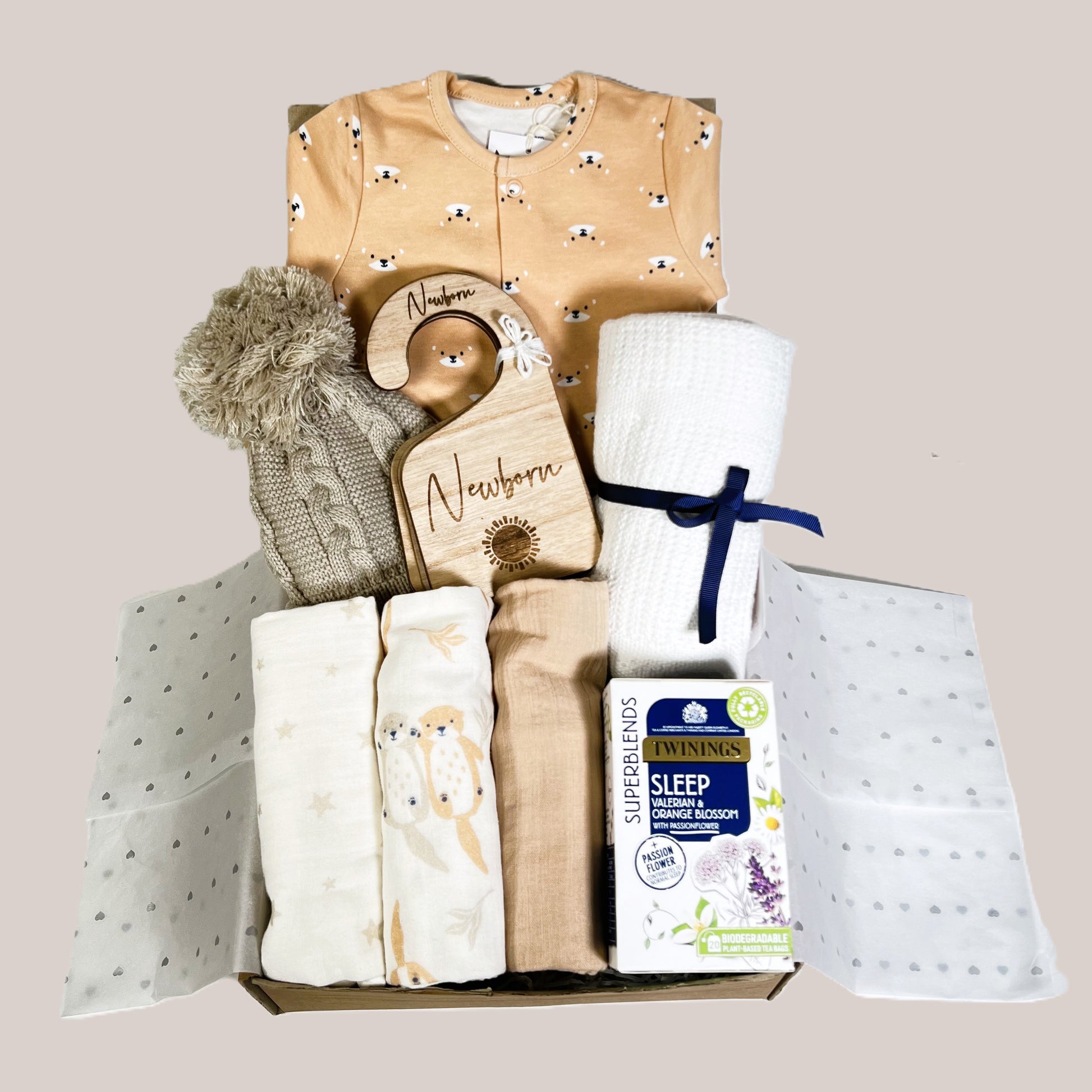 Baby shower gift of a neutral new baby hamper filled with organic cotton new baby essentials including a otter print sleepsuit and a set of three muslin squares.