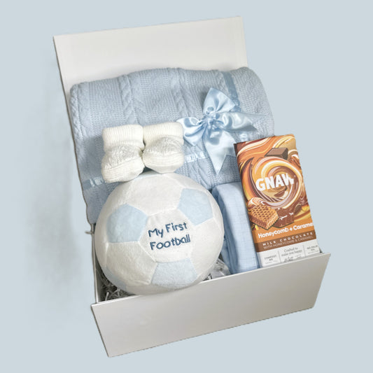 Gift set with 'My First Football', baby blanket, and chocolate bar in a box on a light blue background
