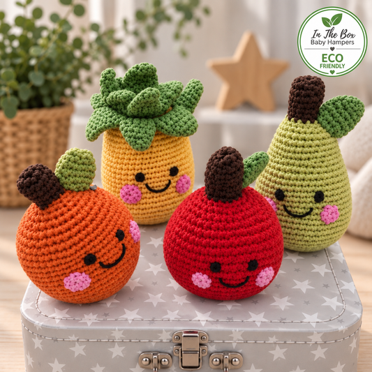 this neutral eco friendly baby hamper gifts contains four crocheted baby rattles an orange, red apple, a yellow pineapple, and a green pear, each with embroidered smiling faces and pink cheeks.