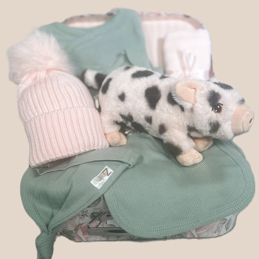 Baby girl hamper with sage green baby clothing, a pink pompom hat and piglet soft baby toy in a keepsake case.