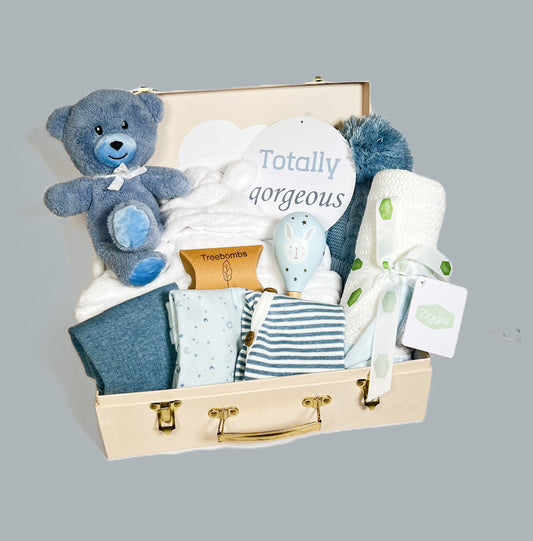 Blue new baby boy hamper in a cream baby keepsake case with a set of blue baby bodysuits, a white cotton cellular baby blanket, a baby rattle, baby hat with pompom and a white baby dressing gown.