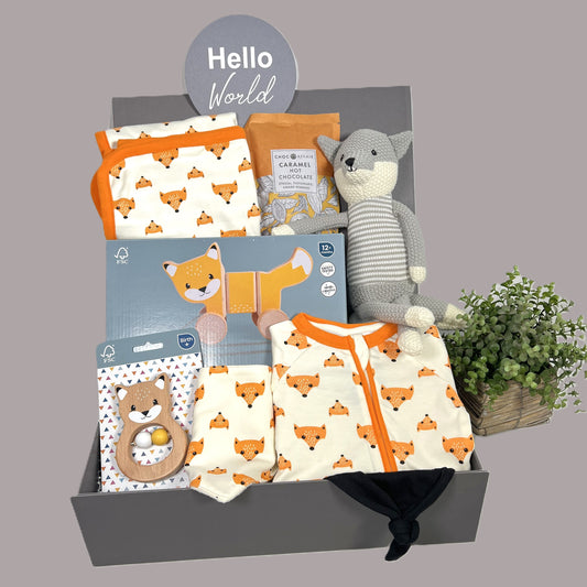 neutral new baby gift fox themed baby hamper with cotton zipped sleepsuit, matching hooded baby blanket and dribble bib, a fox soft toy, a wooden FSC pull along fox toy, a FSC fox baby rattle, a black baby knot hat and a pack of Choc Affair caramel hot chocolate.