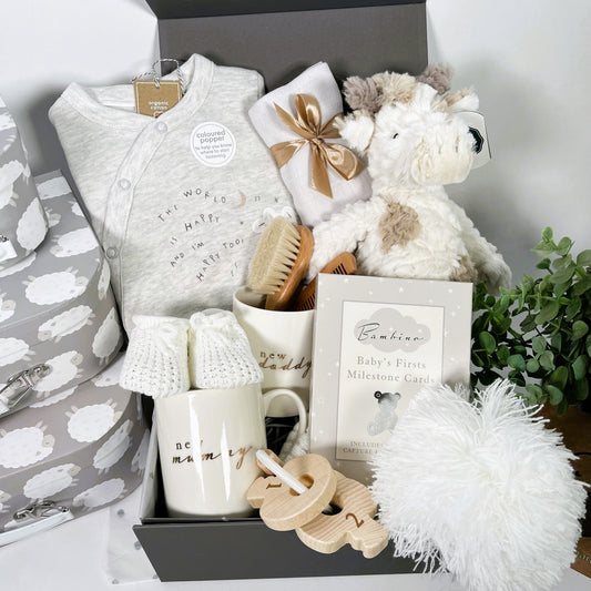 New parent unisex neutral new baby gift hamper box including new mummy and daddy mugs, a Msry Meyer giraffe soft baby toy, a neutral organic cotton baby sleep suit, some baby milestone cards, a baby booties, bambino teething keys and a wooden baby hairbrush and comb set.