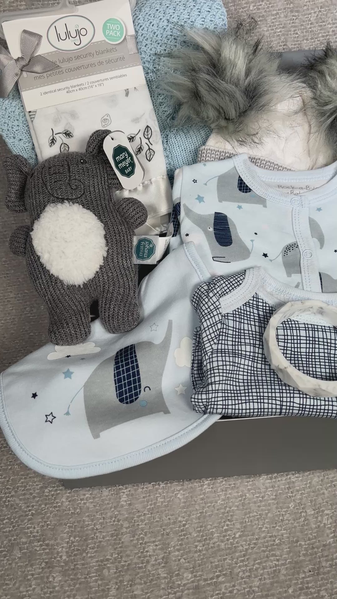 Video of an elephant themed baby hamper with cotton babywear, a baby hat, a blue cotton blanket, a baby rattle and two  security blankets.