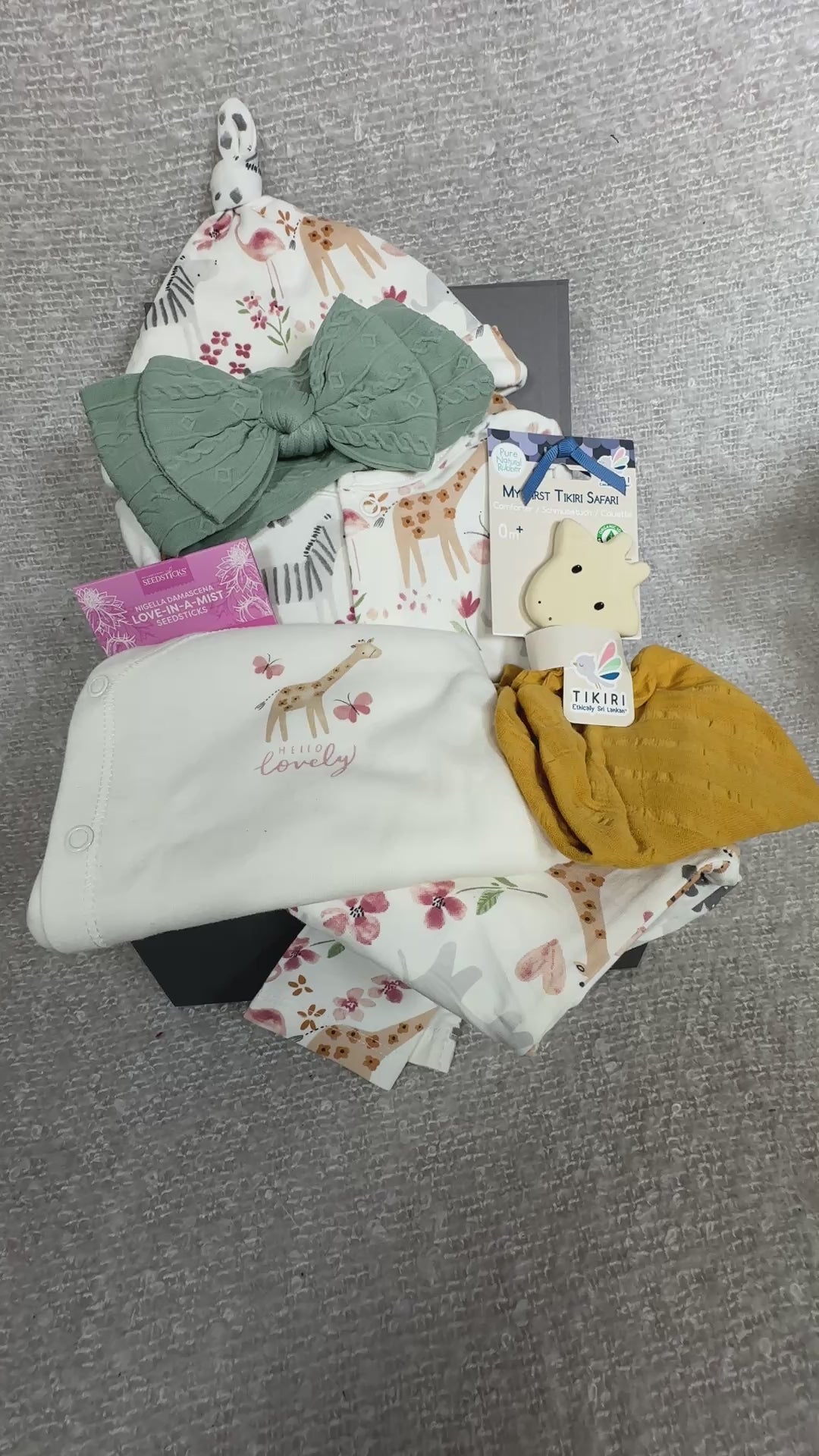Video of a new baby girl hamper with cotton baby sleepsuit, giraffe baby teether and green baby headband.