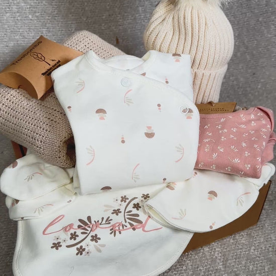 Video of a baby girl hamper with baby clothes, hat, and blanket on a brown background