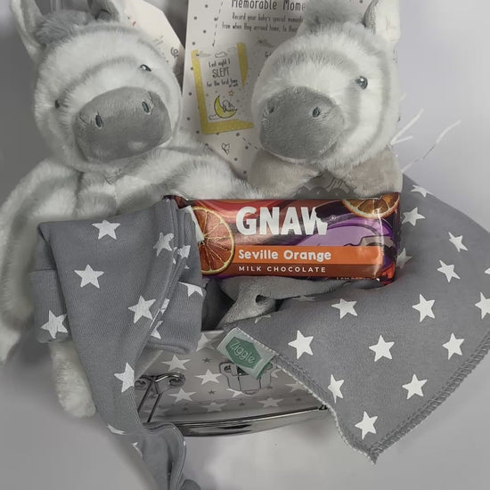 A baby keepsake case with two Keeleco zebra baby toy, a bar of seville orange Gnaw chocolate, a bay knot hat and bib.