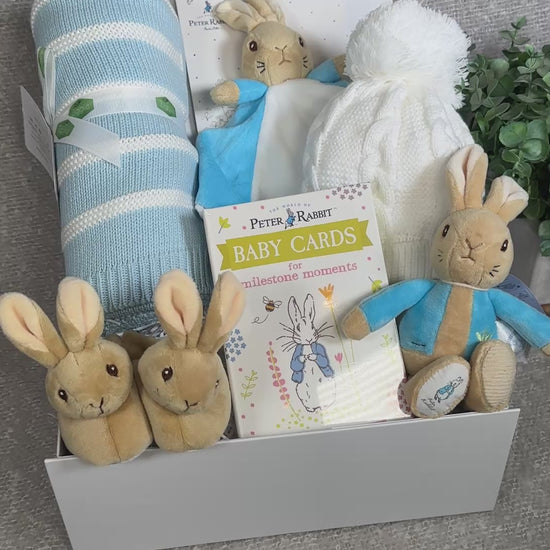 Video of aby gift hamper with peter Rabbit plush toys and baby items on a light blue background