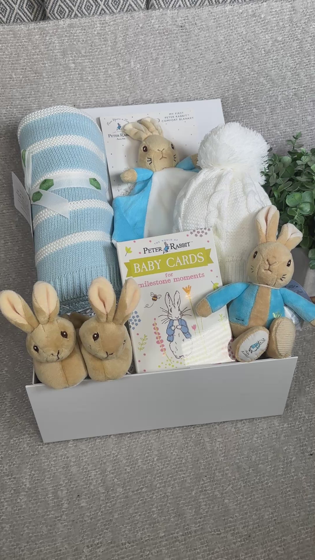 Video of aby gift hamper with peter Rabbit plush toys and baby items on a light blue background