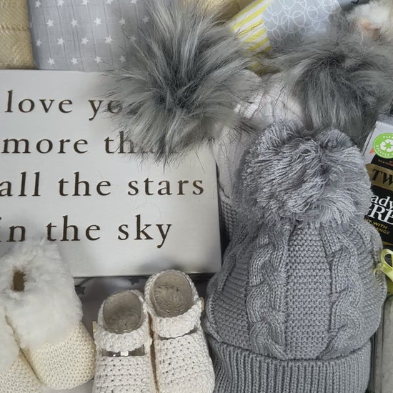 Video of a yellow and white baby gift hamper basket with baby clothes, baby soft toy, tea, baby blanket and baby shoes.