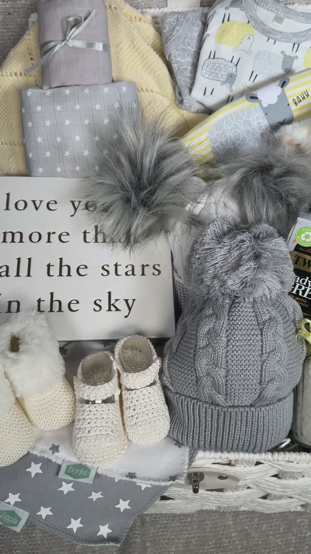 Video of a yellow and white baby gift hamper basket with baby clothes, baby soft toy, tea, baby blanket and baby shoes.