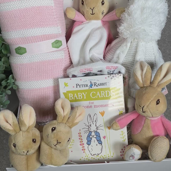 Video of a baby gift hamper with Flopsey bunny  plush toys, blanket, and baby cards on a light pink background