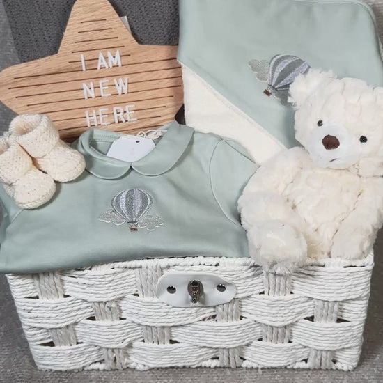 video of a luxury baby hamper in a white paper rope hamper , with sage green baby clothing, hooded baby towel, baby blanket and baby booties