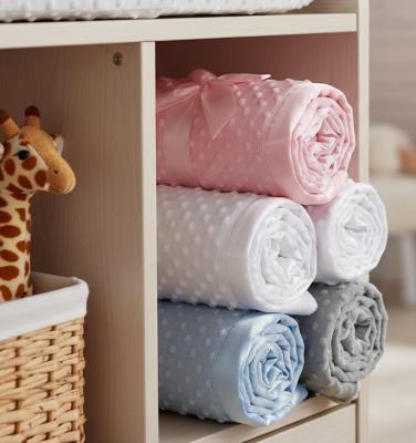Stack of folded dimple  baby blankets in pink, white, blue, and grey with satin trim