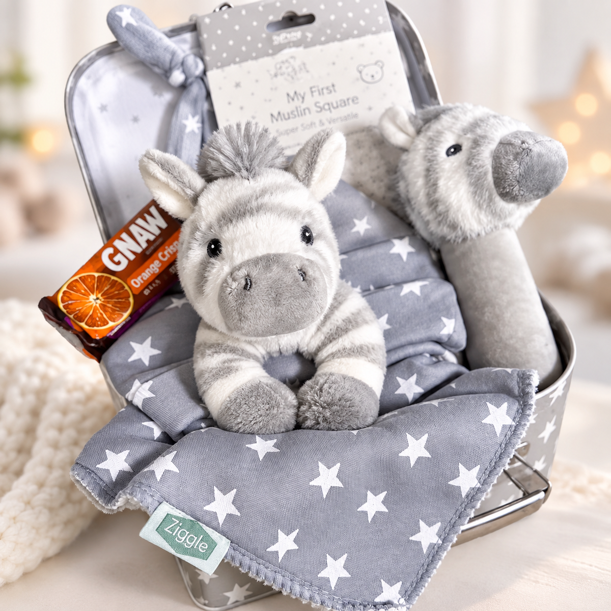 Unisex baby hamper grey and white with Zebra  plush toys, baby hat, and a chocolate bar on a grey background