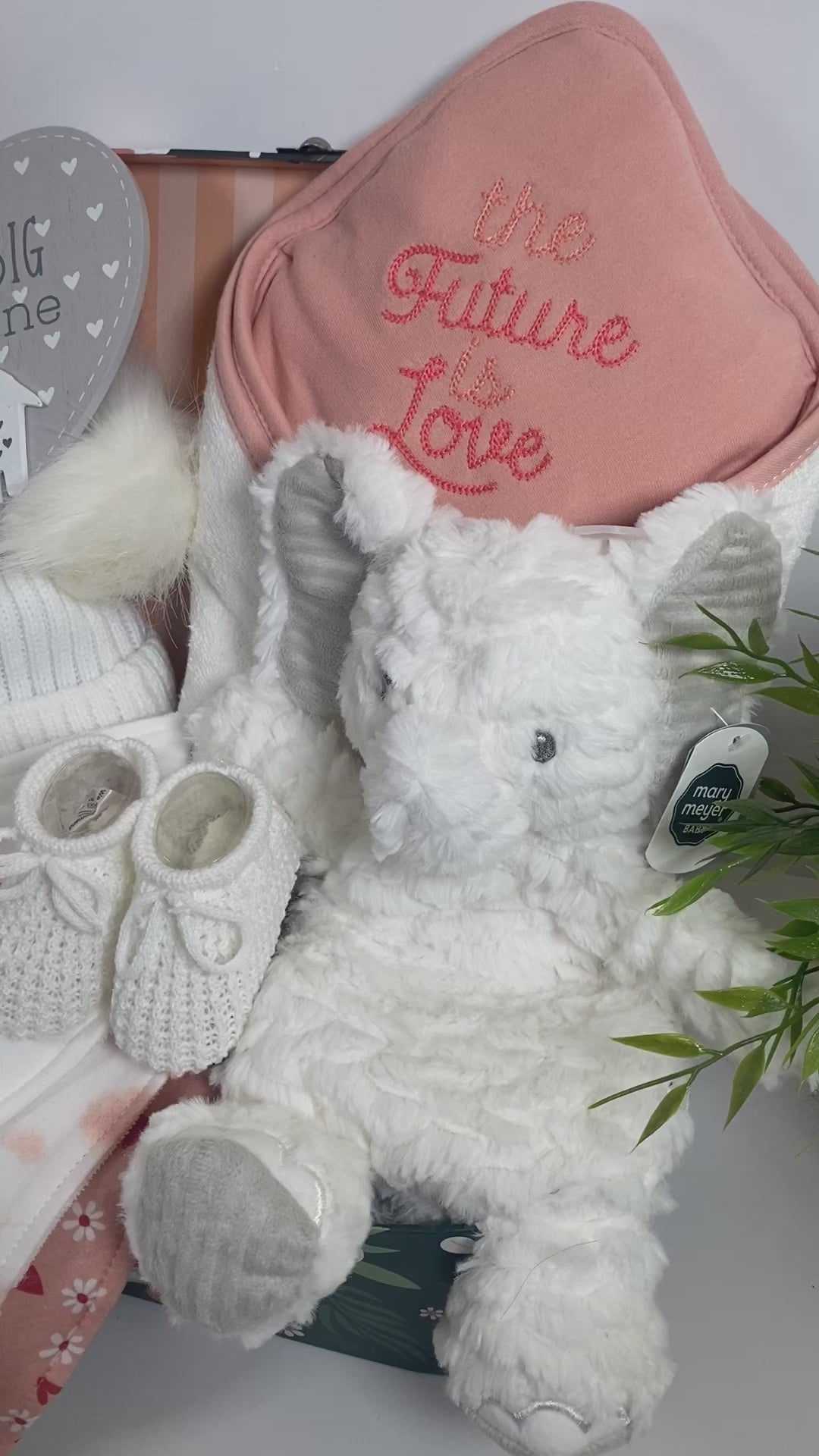 A gorgous floral baby keepsake case contains everything in the new baby girl hamper which contains an organic cotton hooded baby towel in white and peach with the embroidered words "The future is love". A set of 3 matching organic cotton baby bibs in white and peach, a white baby double pom pom hat, a pair of white baby booties, a "Dream big little one" heart shaped nursery plaque with a wooden elephant and a Mary Meyer elephant Lovey.