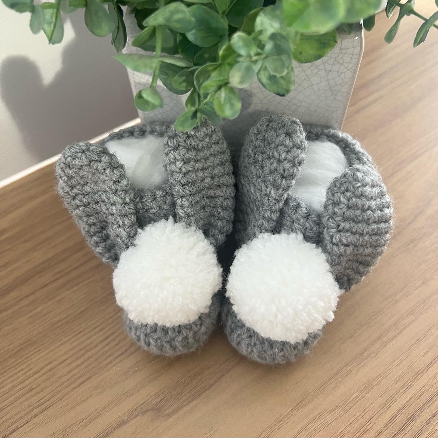 Crocheted baby bootees in grey and white with pom poms and bunny ears.