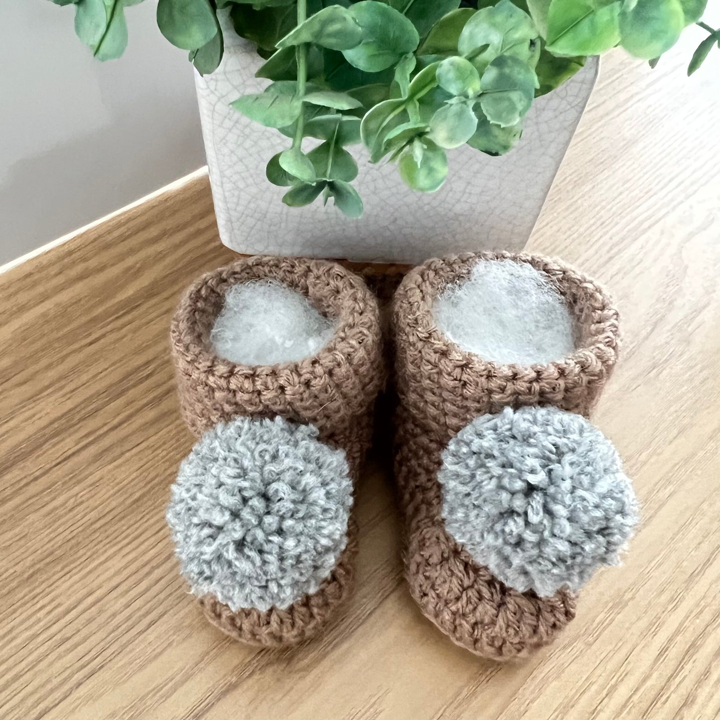baby booties in brown with a grey pom pom.