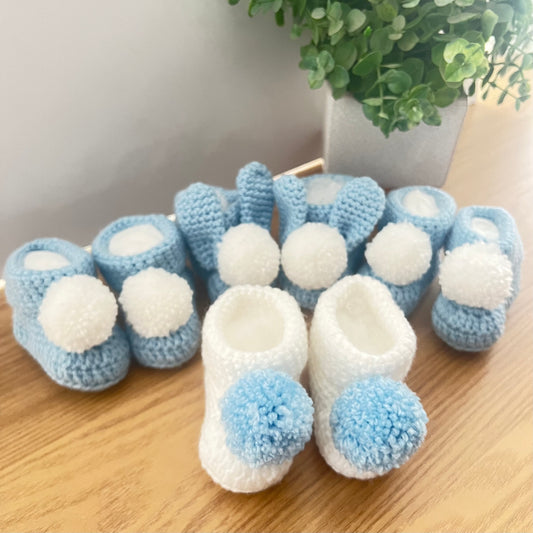 Hand crocheted baby booties with pom poms and some with pom poms and bunny ears - all in blue and white.