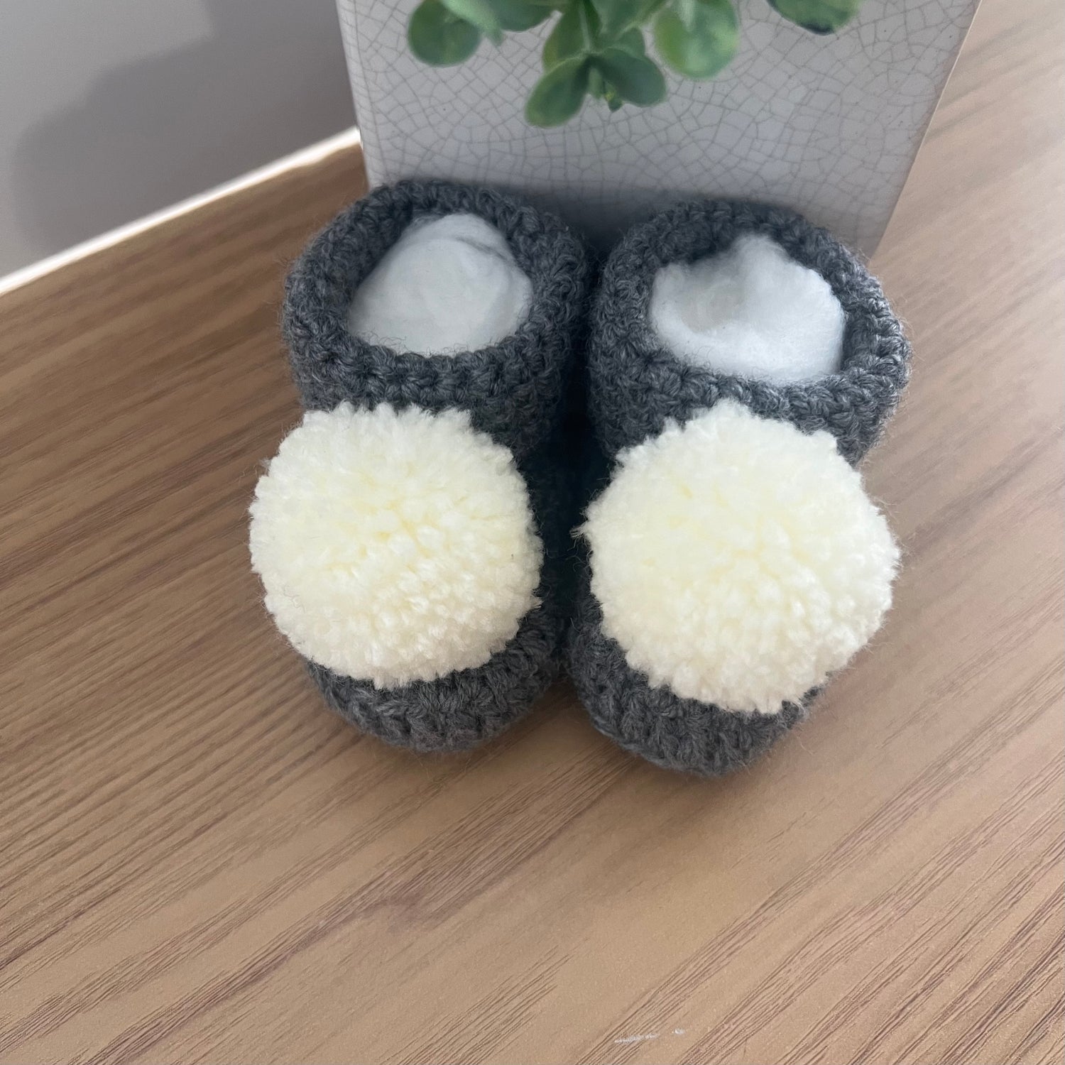 Crocheted baby bootees in grey and white with pom poms