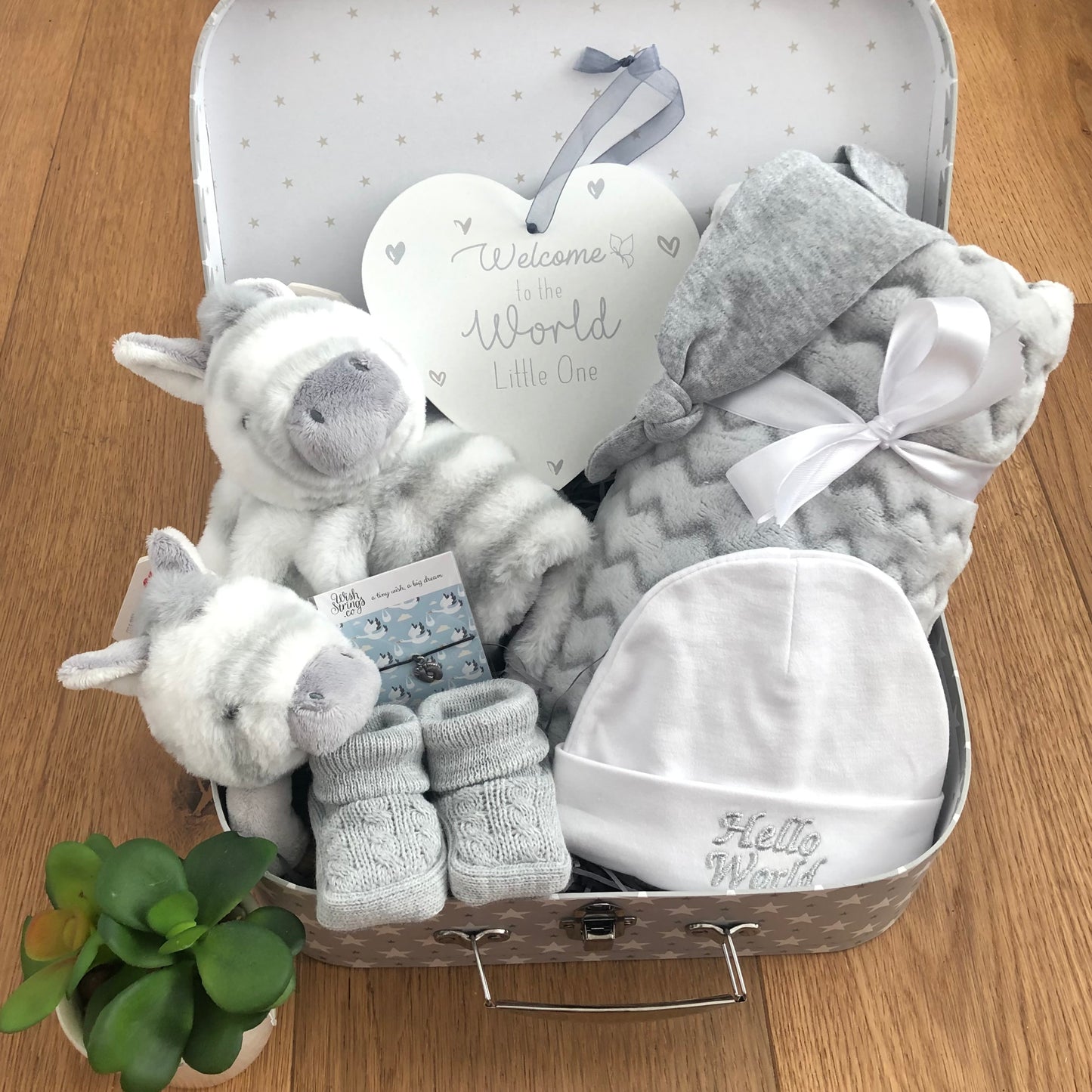 This zebra themed baby hamper comes in a grey and white star patterned baby keepsake case and contains A soft zebra baby comforter, a soft zebra baby rattle on a woooden teething ring, a grey baby blankets with a chevron pettern, a pair of grey baby booties, a wish bracelet, a baby grey knot hat and a white cotton baby hat that has the words "hello world" embroidered on the front and a nursery plaque that says" Welcome to the world little one".